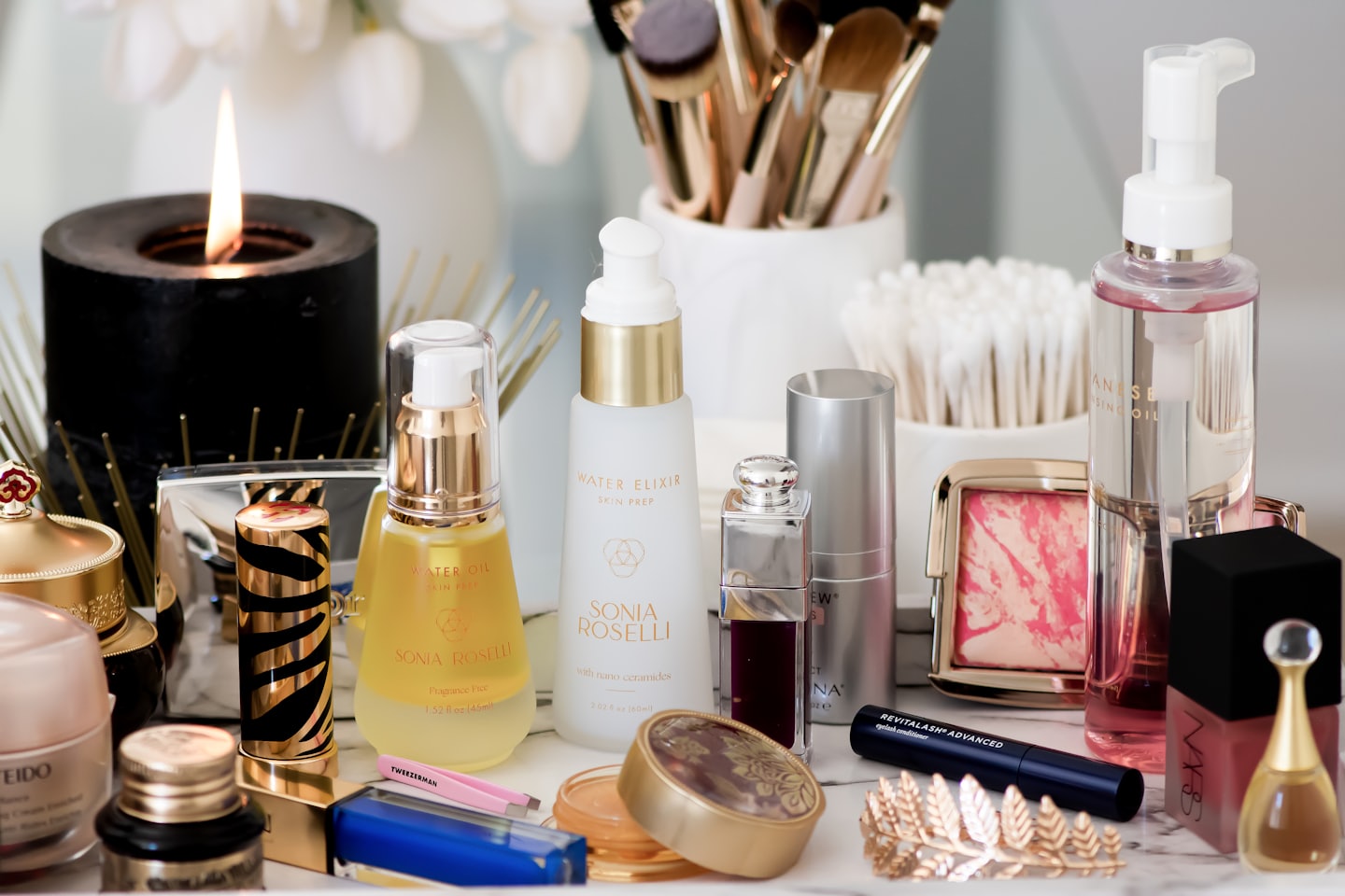 Luxury beauty products arranged with a candle and brushes on a marble vanity.